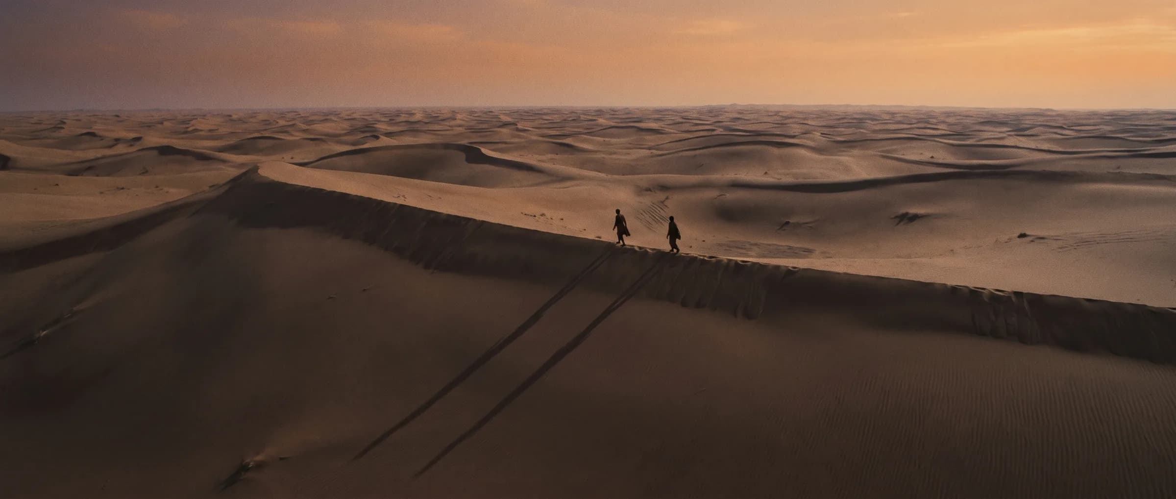 Dunas del desierto al atardecer con dos viajeros a lo lejos